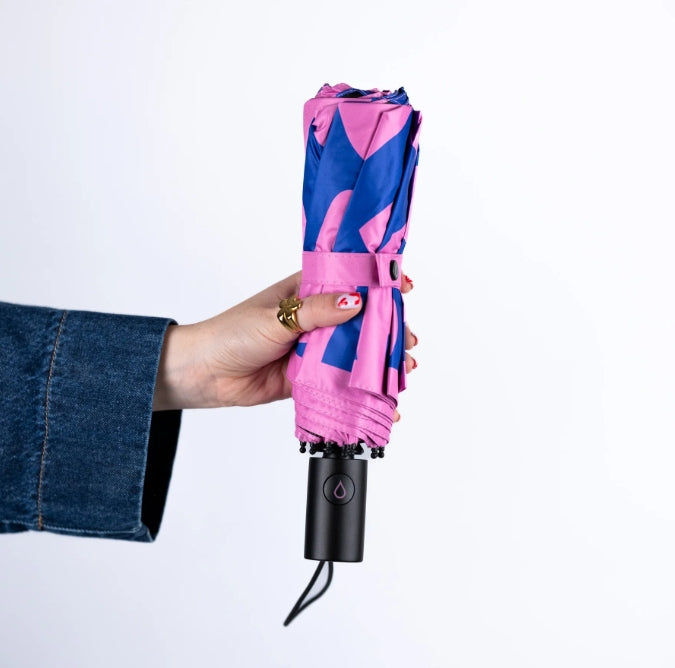 Hand holding a pink and blue umbrella with a black handle on a white background