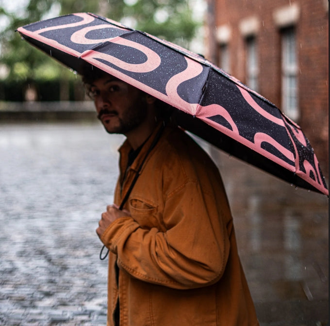Person holding a black and pink umbrella in a rainy street.