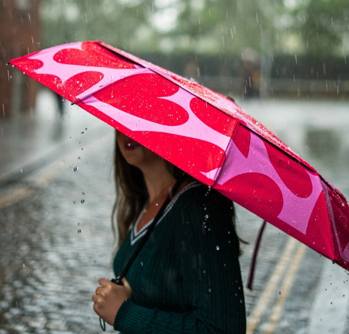 Person holding a pink umbrella with red hearts in the rain
