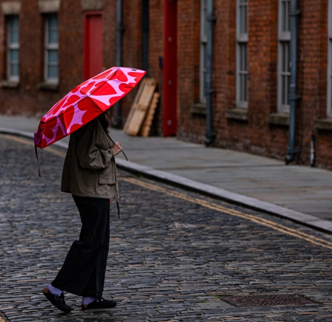 Person walking down a brick-lined street holding a red umbrella with a white pattern.