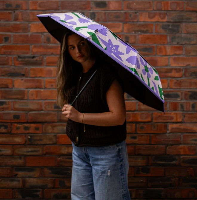 Person holding a floral-patterned umbrella against a brick wall